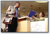 Two people talking, one behind a desk so it looks like he/she is helping the other.